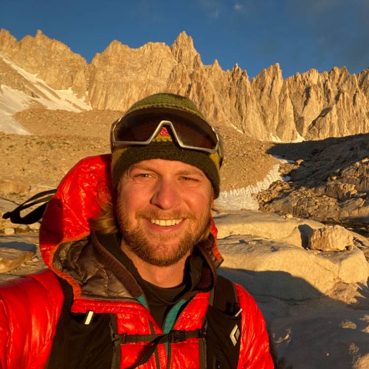John in the mountains with a red jacket and beanie