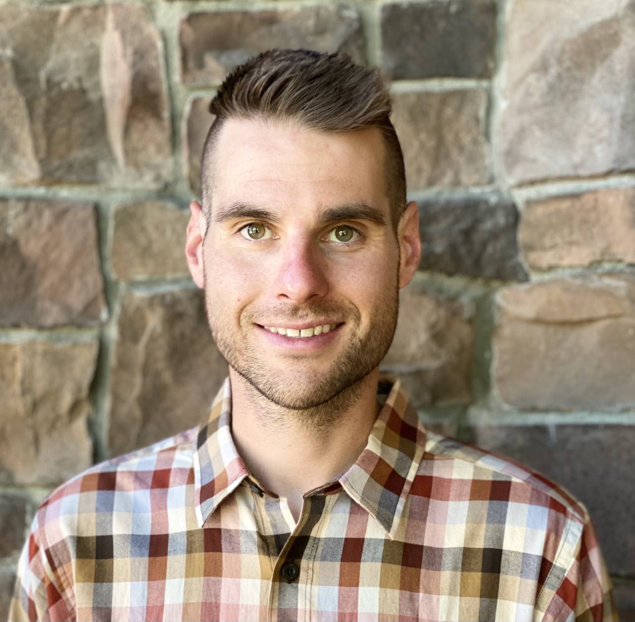 Nicholas standing in front of a stone building wearing a brown plaid shirt